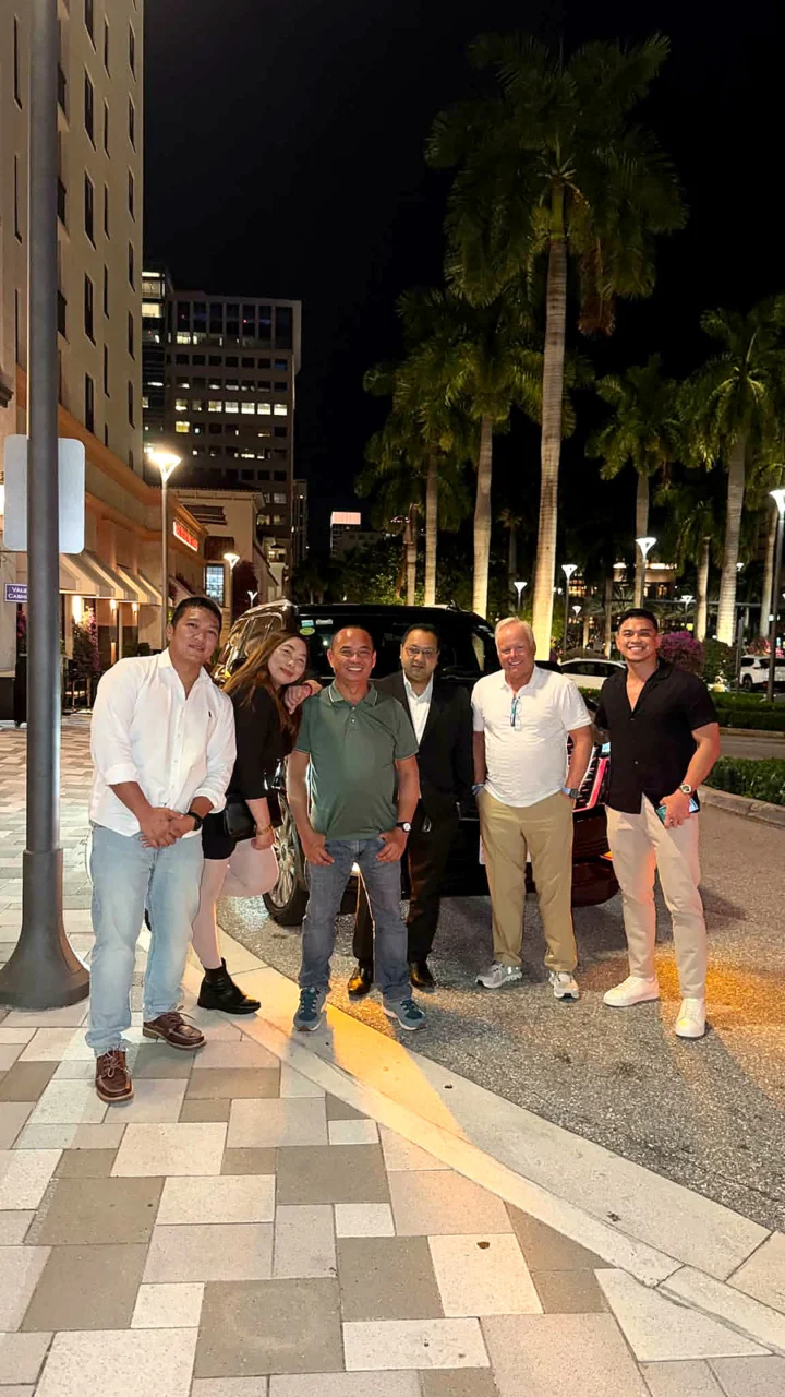 A group of guests standing with a luxury vehicle during an evening out.